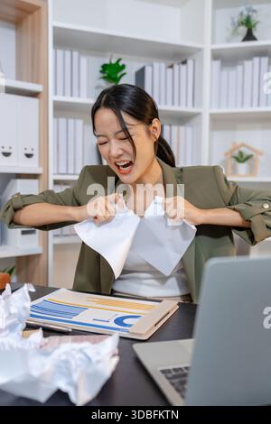 Stressed businesswoman dealing with heavy work pressure, reacting emotionally while reviewing reports and facing tight deadlines, highlighting workpla Stock Photo