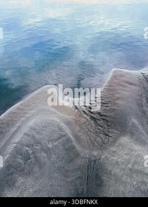 Abstract landscape, beautiful wave-like patterns in the sand where it meets water. Stock Photo