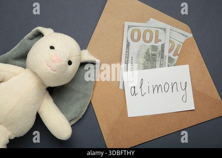 Toy bunny and envelope with word Alimony and money on dark blue background. Top view Stock Photo