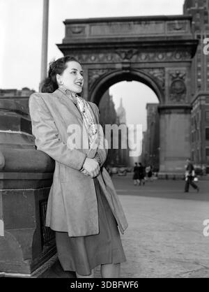 Portrait of Ann Hathaway, Washington Square, New York,   N.Y., ca. May 1947  -  Ann Hathaway poses with a background of the Arch of Triumph in Washington Square, through which may be seen the Fifth Avenue skyline and a glimpse of the Empire State building. Stock Photo