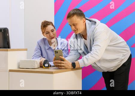 Smiling woman places scanner on box while man holds phone over desk. Stock Photo
