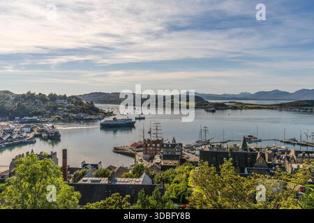 A panoramic view of Oban Bay in Scotland, showing boats, a bustling harbor, historic stone buildings, and green hills. Ideal for travel, coastal life, Stock Photo