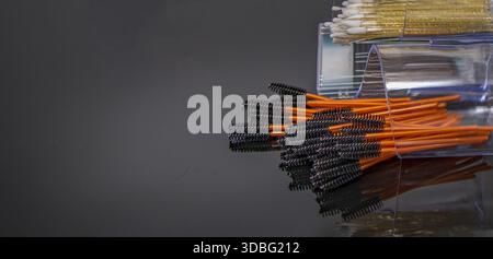 Disposable mascara brushes in transparent containers on reflective studio surface Stock Photo