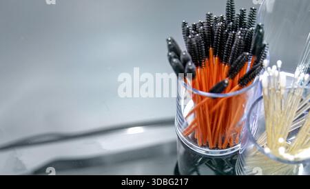 Disposable mascara brushes in transparent containers on reflective studio surface Stock Photo