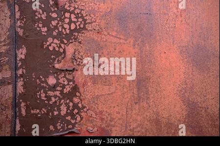 Extreme close-up of metal panel showing heavy corrosion, layered peeling paint in brown and red tones, pitted texture, natural light, flat angle. Stock Photo