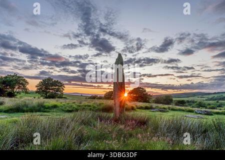 A solitary standing stone amid rolling green fields, with a vibrant sunset and dramatic clouds over Arran's countryside. A historic stone circle captu Stock Photo