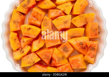 Pumpkin cut into pieces with sugar and cinnamon in a ceramic dish, ready to bake on a white background, close-up, top view. Stock Photo