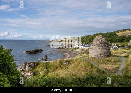 Coastal scene of Dunure harbour with a round stone tower, village houses, and rocky shoreline. Stock Photo