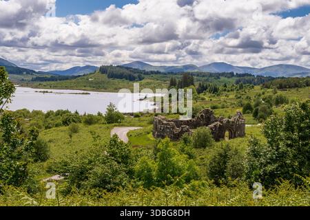 Ancient castle ruins beside a lake with rolling hills and lush greenery in Scotland. Stock Photo