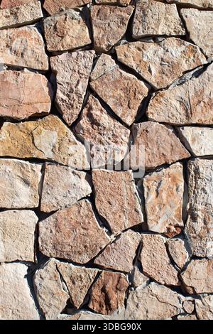 Close-up of an irregular natural stone wall with visible mortar lines and warm earth tones Stock Photo