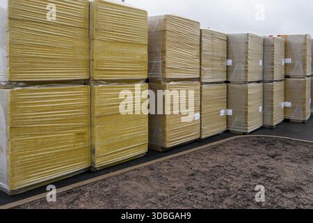 Pallets of insulation panels wrapped in plastic and stored outdoors at a construction site, showing building materials prepared for construction use Stock Photo