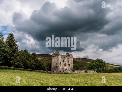 Ancient stone tower ruins sit in a green field with dark storm clouds overhead, dramatically. Stock Photo