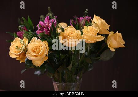 A vibrant floral bouquet featuring soft yellow roses and bright magenta flowers arranged in a clear glass vase against a dark background. Stock Photo
