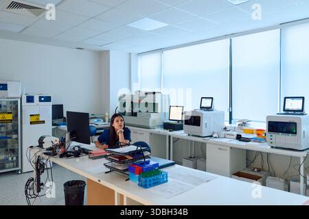 Laboratory setting featuring a female scientist engaged in research work amid advanced equipment and a clean workspace during daylight hours Stock Photo