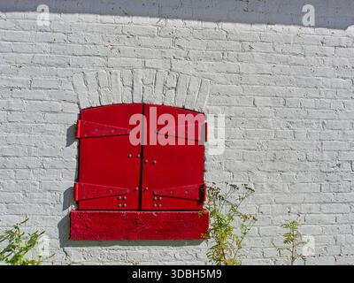 Red shuttered window on white brick masonry wall at Sturgeon Point Light Station Stock Photo