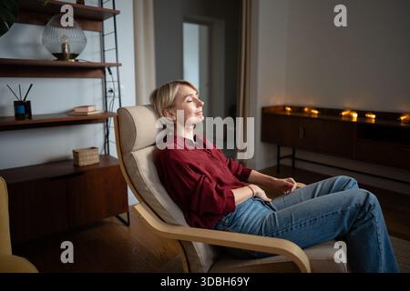 Tranquil relaxed middle aged woman resting at home in comfy chair, dreaming enjoying calm moments. Stock Photo