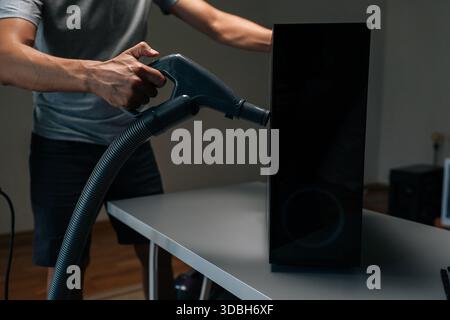 Side view of technician using vacuum cleaner to remove dust and debris from ventilation holes of computer case, performing important maintenance Stock Photo