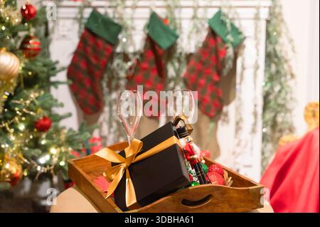 Holiday toast tray with wrapped gift, two empty champagne flutes, decorative nutcracker and ornaments placed on cushioned ottoman in front of stocking Stock Photo
