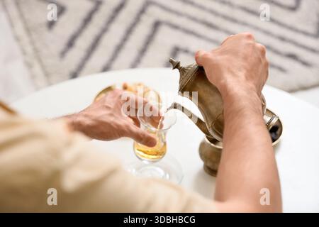 Young man pouring Turkish tea into glass on table at home, closeup Stock Photo