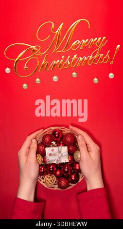 A wicker basket filled with red and gold Christmas ornaments and a gift box placed on a vibrant red background. Stock Photo