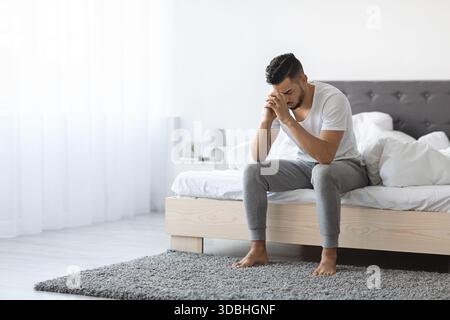 Young Arab Man Sitting on Bed Looking Distressed in a Quiet Room Stock Photo