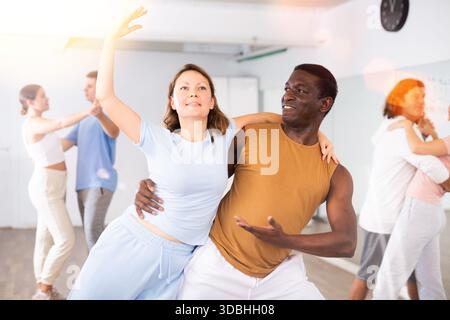 Smiling young adult couples dancing together in pairs and practicing new movements in modern studio Stock Photo