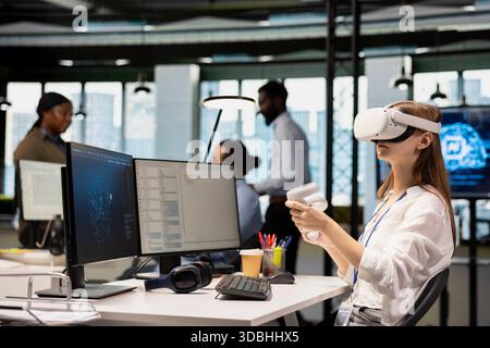 Female engineer wearing VR goggles coding with AI language model assistance in startup office. Young IT professional using virtual reality integrating LLM assistant suggestions into code editor Stock Photo