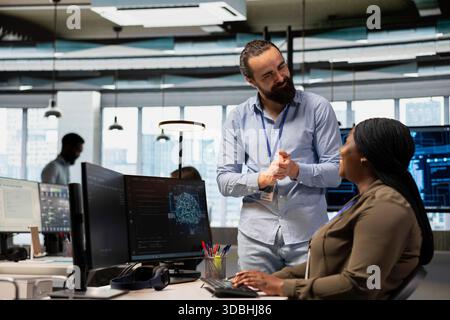 Pleased tech company manager applauding female programmer for optimizing code using AI. Satisfied team leader offering positive feedback to work done by african american woman in office Stock Photo
