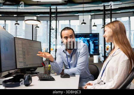 Happy IT professional teaching intern to use artificial intelligence. Smiling team leader programmer guiding junior dev through AI tool integration, mentoring her on using machine learning APIs Stock Photo