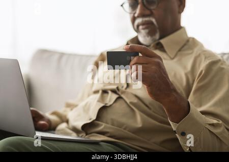 Older Man Using Contactless Card Technology at Home While Accessing Information on Laptop Stock Photo