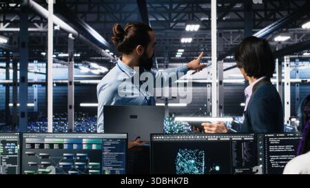 Team of engineers doing brainstorming in server room using AI to review infrastructure diagnostics. Teamworking IT colleagues in data center analyzing data using artificial intelligence, camera A Stock Photo