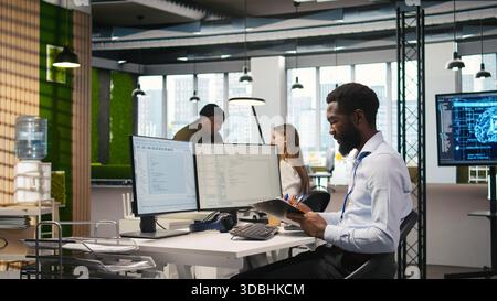 Admin in tech startup office using PC, compiling software patches to fix bugs, troubleshooting backend operations. IT expert running diagnostics, resolving system crashes via terminal, camera A Stock Photo