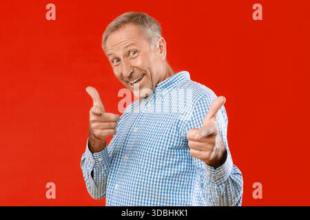 Older Man Smiling and Posing With Hand Gestures Against a Red Background Stock Photo