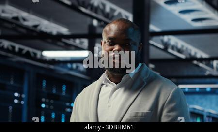 Server farm admin overseeing supercomputers, troubleshooting bugs. African american manager walking in data center, doing inspection to ensure error free equipment, camera B Stock Photo