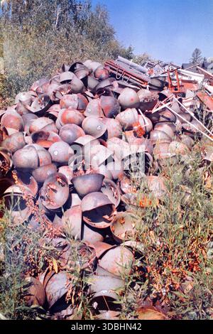 Pile of discarded Yugoslav Army helmets at a military scrapyard, sunlit scene captured on analog 35mm film. Stock Photo