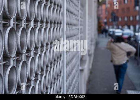A blurred figure walking past a textured metal wall with circular patterns, urban setting of Milan, Italy Stock Photo