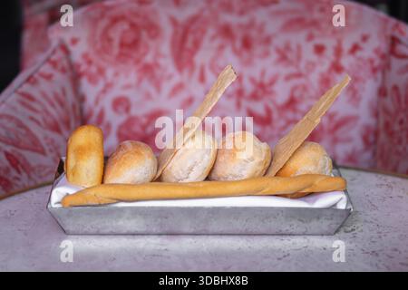 A metal tray filled with various types of bread, including rolls and breadsticks, arranged neatly on a white cloth Stock Photo