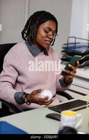 Young Adult Black Man Sitting at Desk Using Smartphone and Holding Baseball Stock Photo
