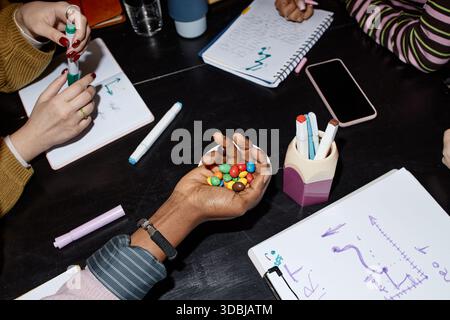 Multiethnic Young Adults Collaborating While Sharing Candy during Meeting Stock Photo