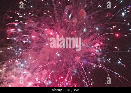 Pink and red fireworks fill the night sky over Huntington Beach, California, creating a vibrant celebration with sparkling trails and glowing smoke. Stock Photo