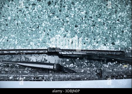 Close-up view of a car windshield covered in hailstones and ice pellets, with wet windshield wipers visible during an intense weather event and cold Stock Photo