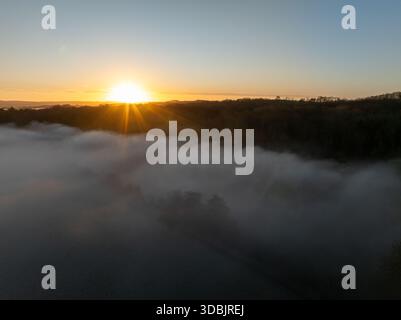 Aerial view of a tranquil, mist-laden valley bathed in the radiant glow of the rising sun, silhouetting the distant treeline, Thames Valley, Oxfordshi Stock Photo