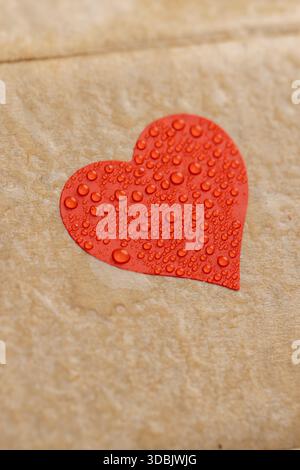 wet cardboard for packaging goods and products with red plastic hearts glued on , cardboard with red hearts covered with water droplets Stock Photo