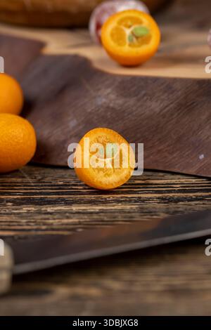 cut ripe orange kumquat cut in half on a wooden table, a group of scattered and sliced kumquat fruits on a wooden table and board Stock Photo