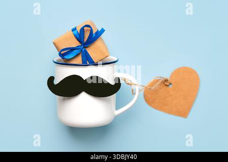 Happy Father's Day. Top view of cup of coffee with false mustache and gift box and heart shaped sales tag over blue background Stock Photo