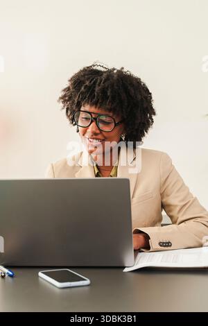 Professional woman is engaged in work on her laptop while dressed in a tailored suit, displaying concentration and dedication at her desk, embodying Stock Photo