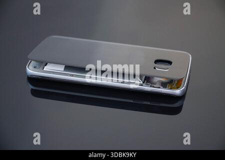 Damaged mobile phone on a black background. Swollen lithium ion polymer battery inside a smartphone. Stock Photo