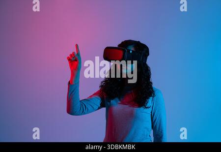Woman using VR headset with neon blue red lighting while interacting with virtual interface in studio scene Stock Photo
