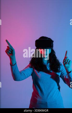 Young woman using VR headset with neon lighting gestures in immersive virtual reality environment Stock Photo