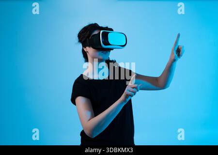 Woman interacting with virtual environment using VR headset and multi-directional gestures on blue background Stock Photo